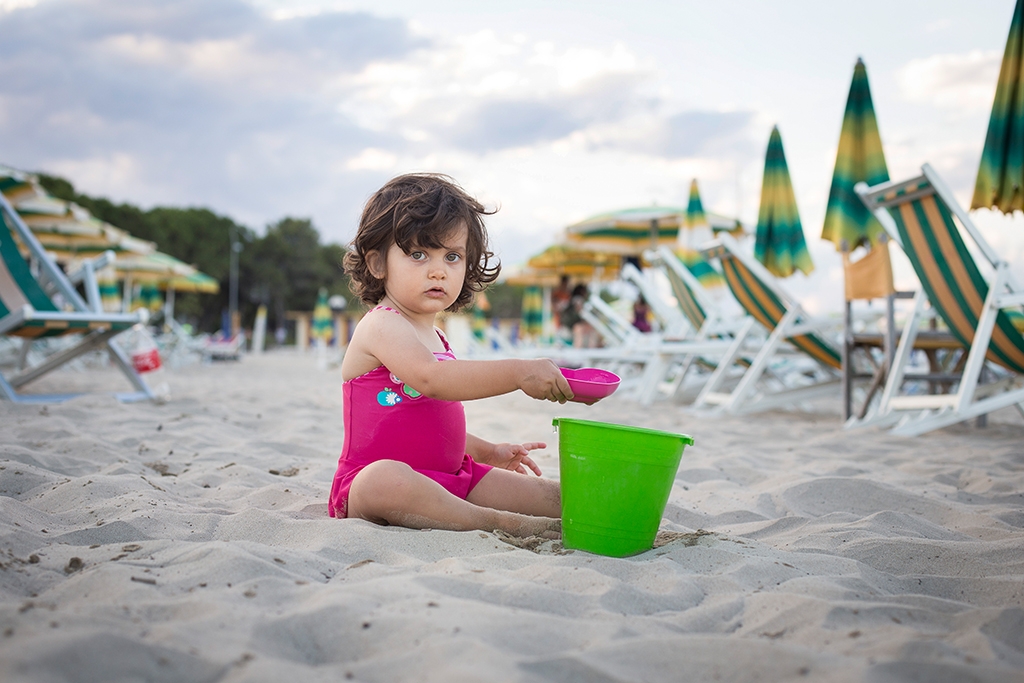 Bambina che gioca con secchiello sulla sabbia