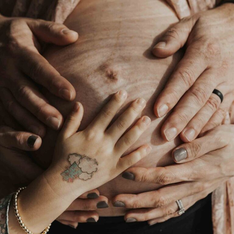 Le mani del papà e della sorellina sulla pancia di una mamma in dolce attesa durante un servizio fotografico di gravidanza Roma