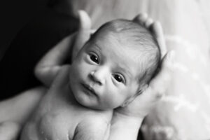 Un bimbo appena nato nelle mani della sua mamma guarda dritto in fotocamera durante un SERVIZIO FOTOGRAFICO NEONATI