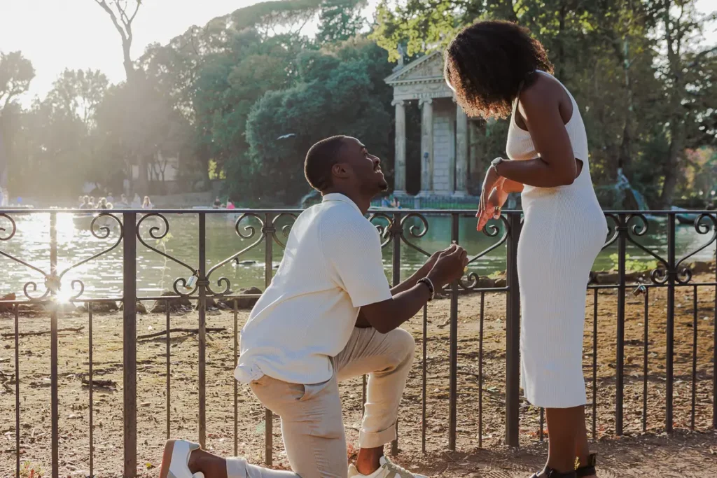 A man on his knees is proposing his girlfriend during a surprise proposal at Villa Borghese